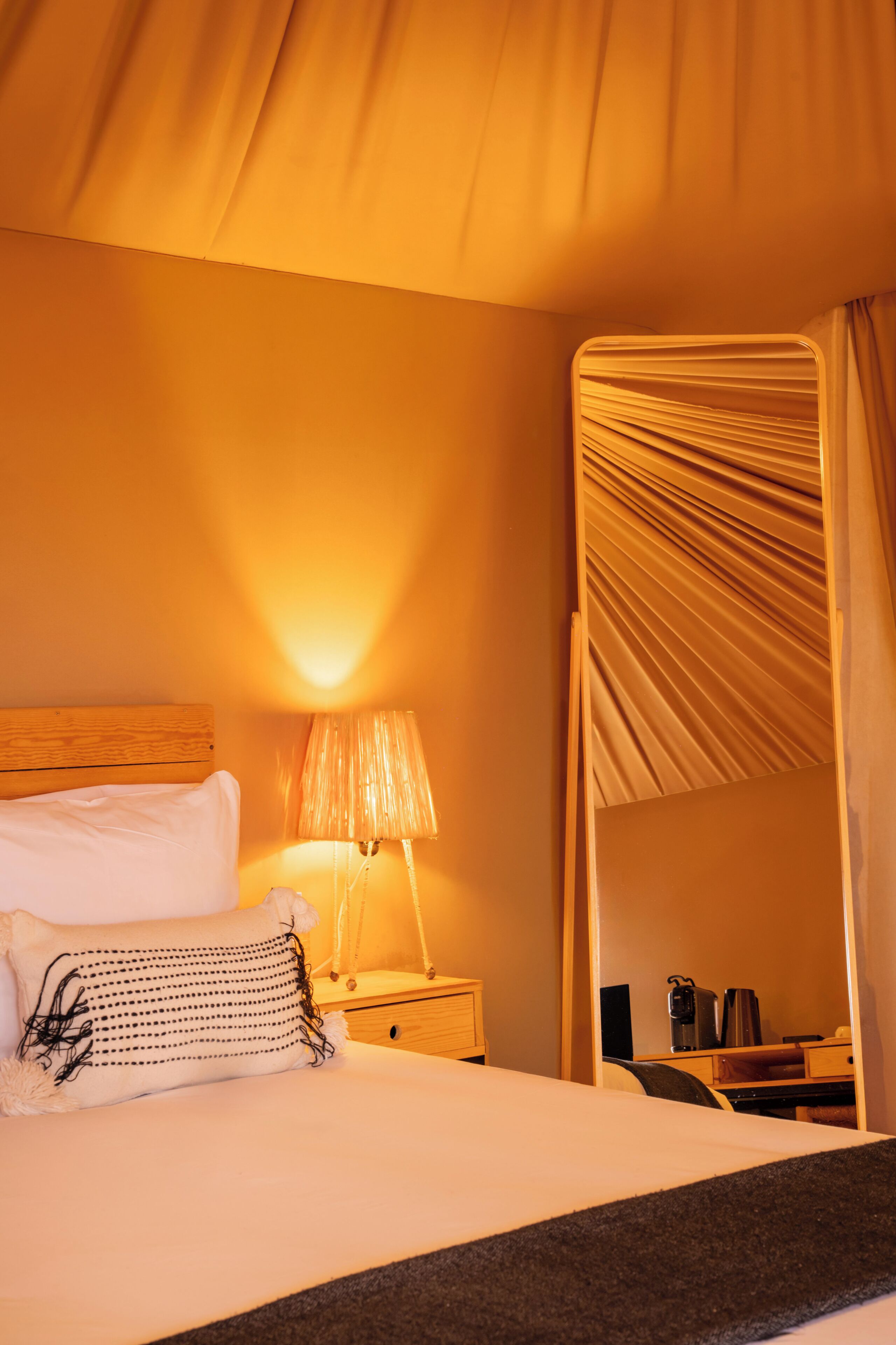 A hotel room with a bed, a bedside lamp, a wooden nightstand, and a mirror.