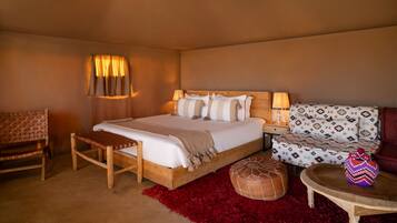 A bedroom with a wooden bed, a red rug, a wooden bench, a patterned sofa, and a small table with a decorative item.