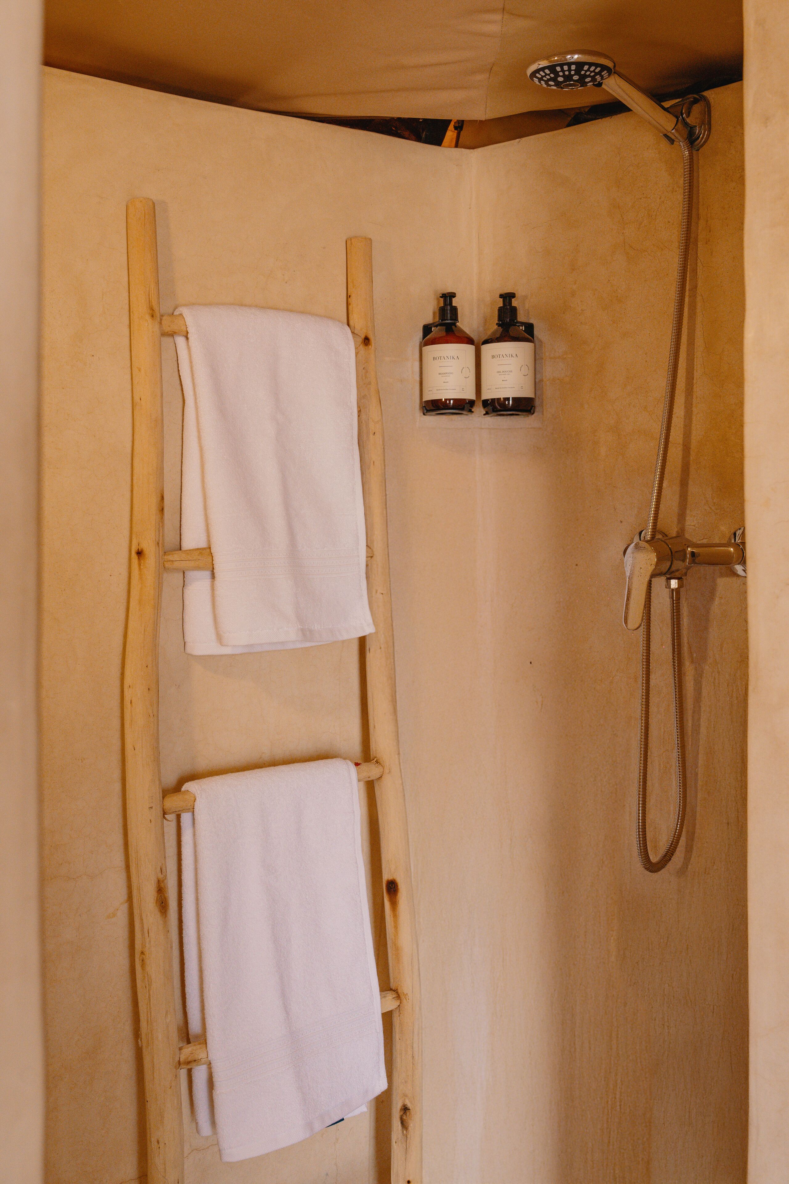 Une échelle en bois sur laquelle sont suspendues deux serviettes blanches, une pomme de douche et deux bouteilles de shampoing accrochées au mur.