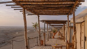 A wooden deck with tables and chairs, surrounded by tents and potted plants, overlooking a desert landscape. - Mia Agafay Resort (Agafay)