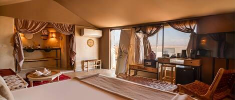 Habitación de hotel con una cama grande, un escritorio, una silla, una mesita y vistas al desierto.