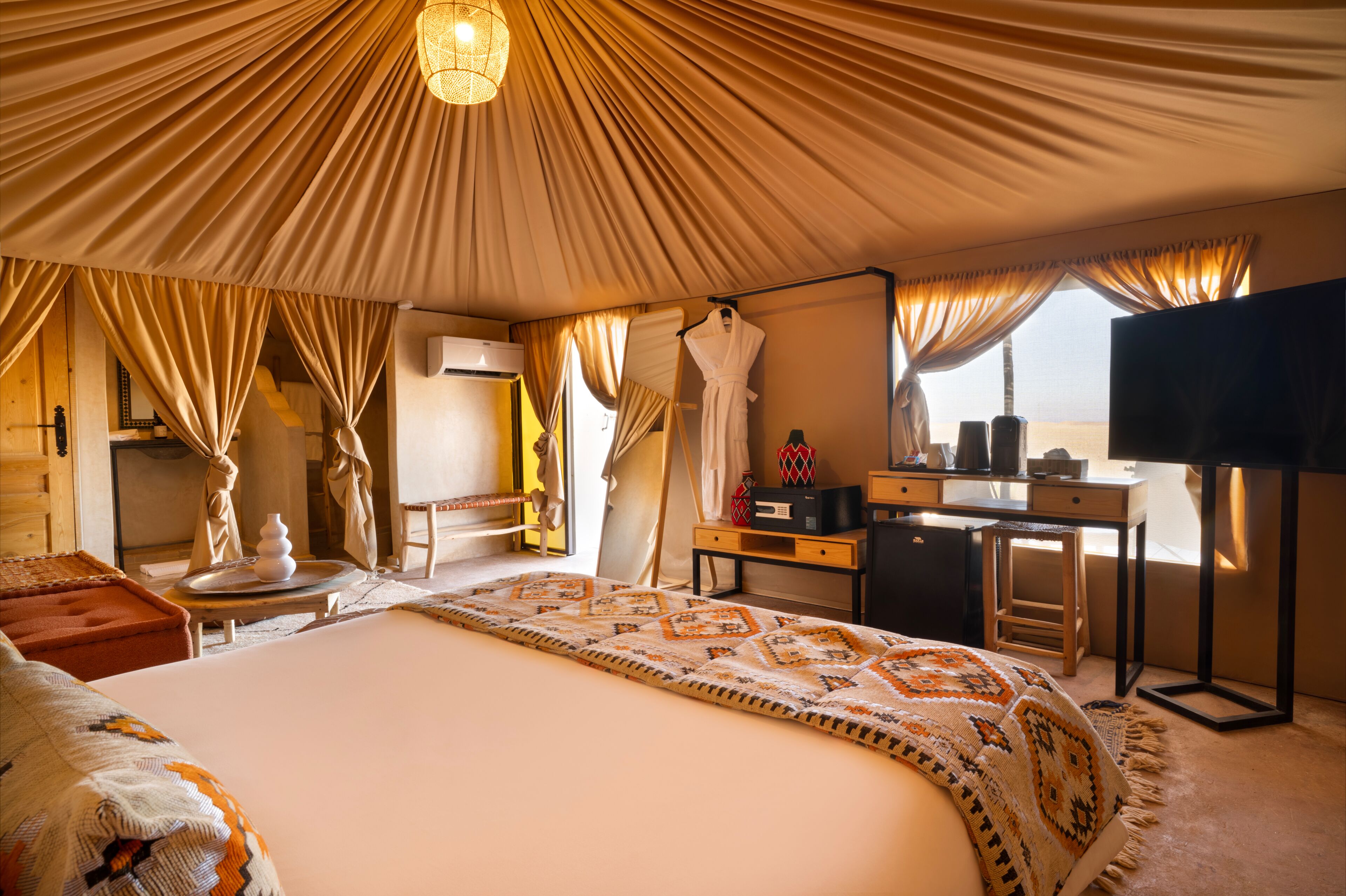 A tent-style room with a bed, desk, and TV.
