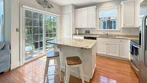 A modern kitchen with white cabinetry, a granite countertop, and a large island with stools. - Relax and recharge in comfort at this stylish Heritage Village retreat! (Lewes)