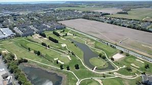 An aerial view of a golf course with a pond, surrounded by residential areas and a bridge. - Relax and recharge in comfort at this stylish Heritage Village retreat! (Lewes)