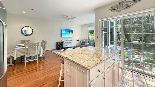 A spacious kitchen with a large island, wooden flooring, and a view through a glass door to the outdoors. - Relax and recharge in comfort at this stylish Heritage Village retreat! (Lewes)