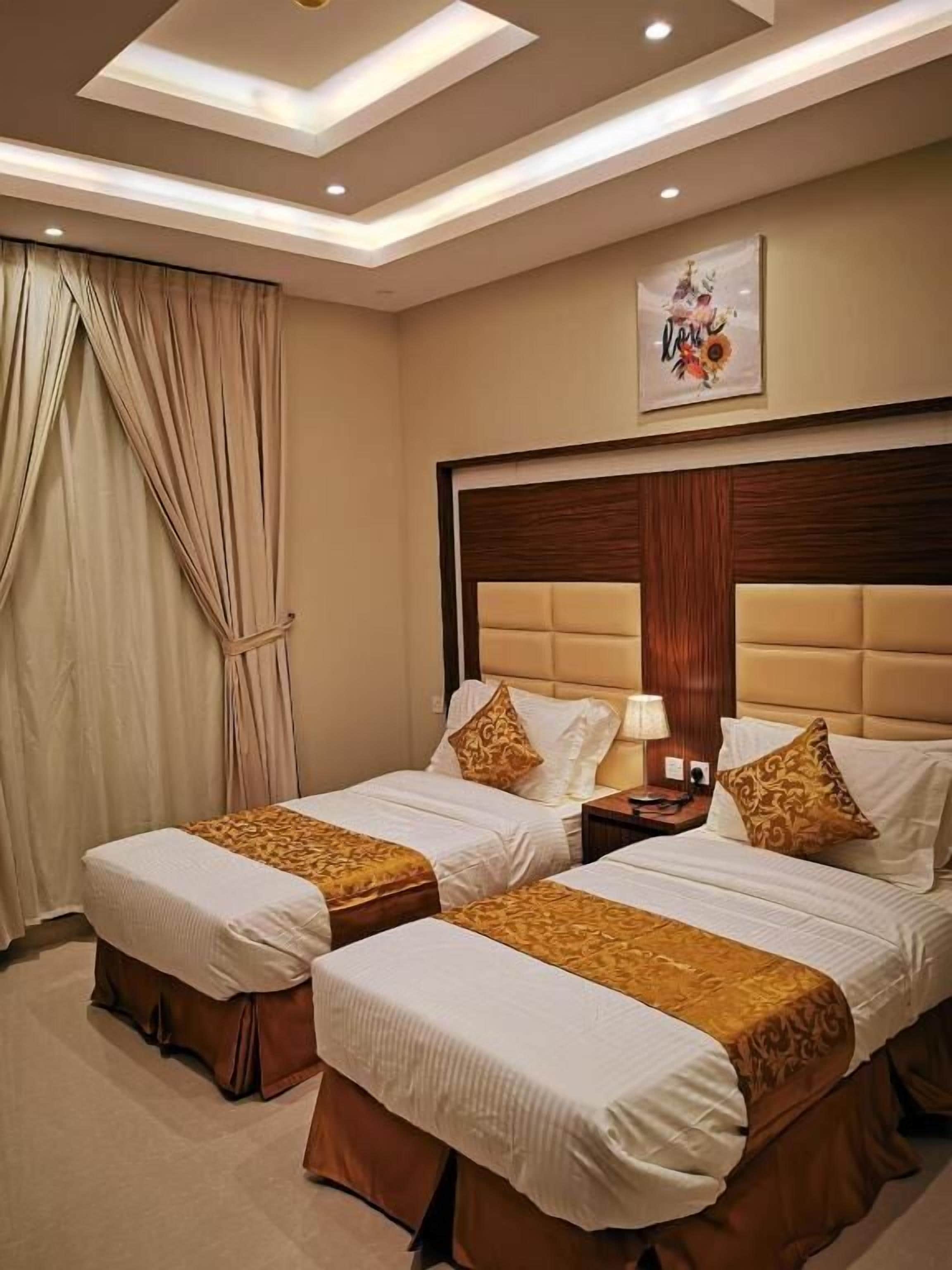 A hotel room with two beds, beige curtains, a wooden headboard, and a framed artwork on the wall.