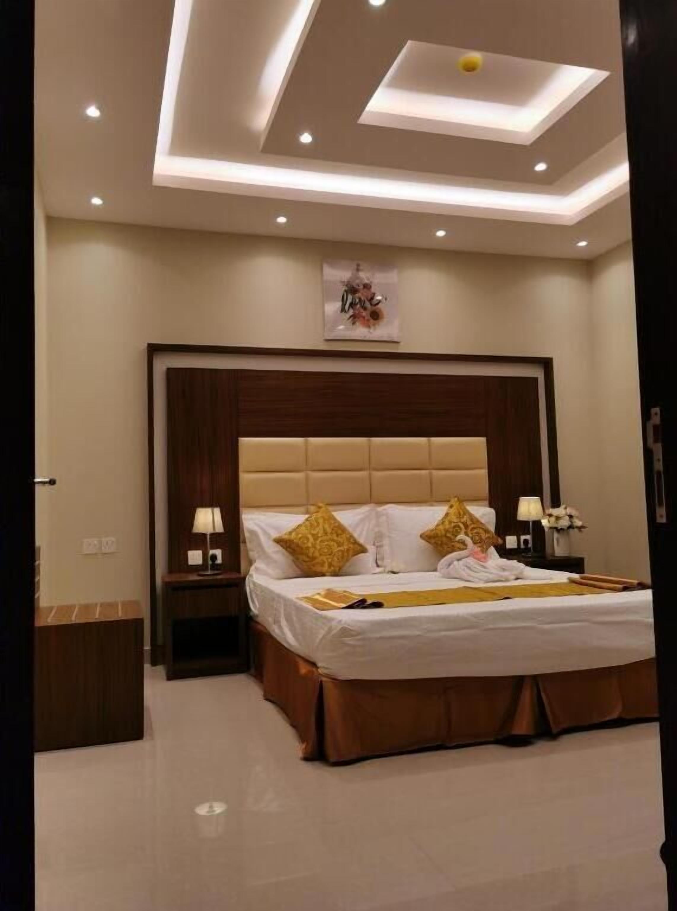 A modern bedroom with a large bed, wooden headboard, and recessed ceiling lighting.