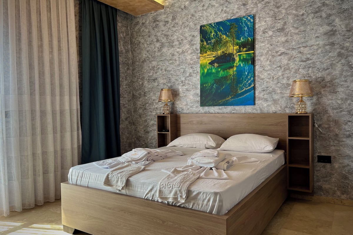 Ein modernes Schlafzimmer mit einem hölzernen Bett, einem großen Gemälde eines Sees und zwei Nachttischlampen.