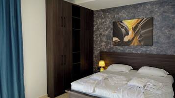 Habitación de hotel con una cama grande, un armario, un cuadro en la pared y una mesita de noche con una lámpara.