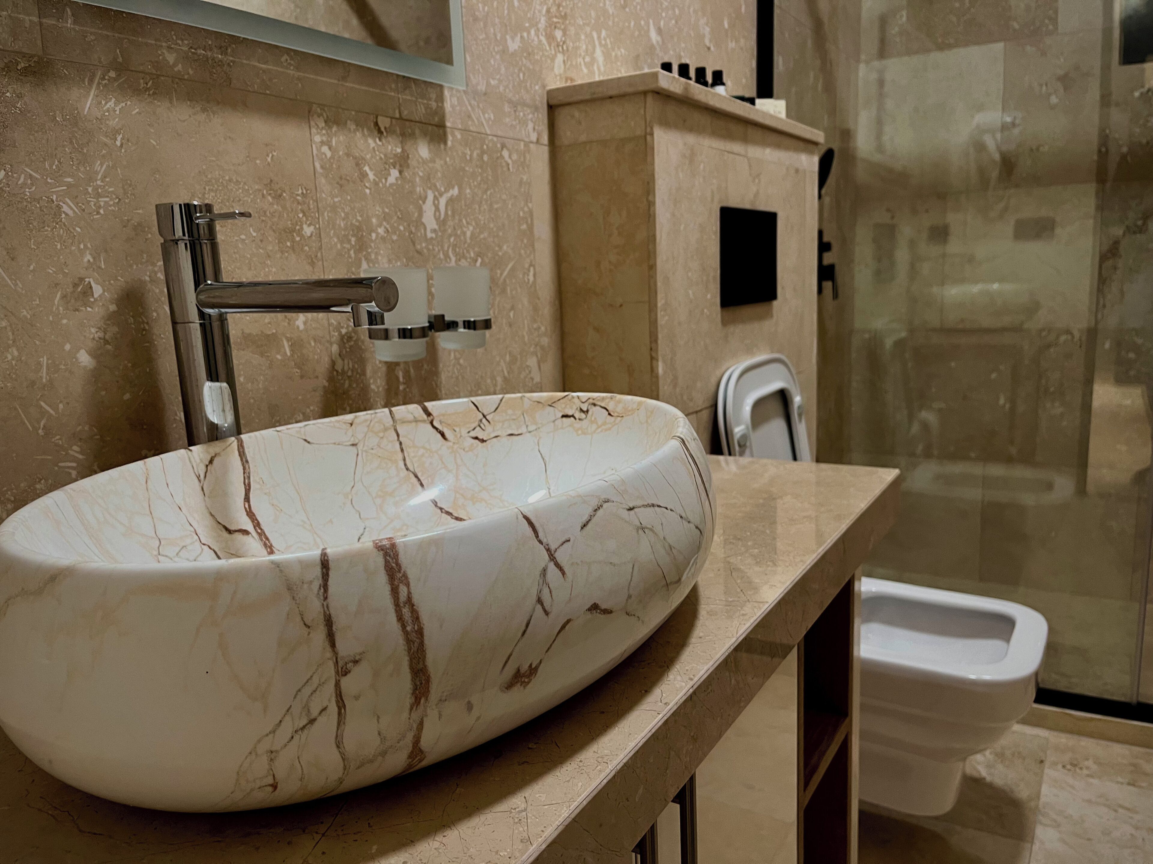 Un bany amb un lavabo de marbre, un aixeta modern, un vàter i un box de dutxa de vidre.