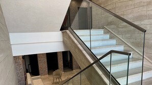 Un intérieur moderne avec un escalier en verre, un coin salon avec un canapé et des fauteuils, et un mur en pierre.