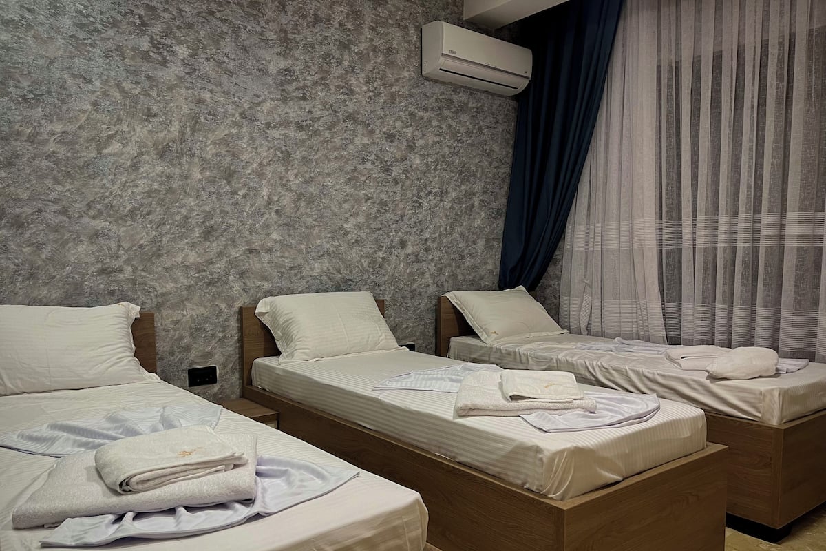 Ein Hotelzimmer mit drei Einzelbetten, jeweils ausgestattet mit einem ordentlich gefalteten Handtuch und Kissen.