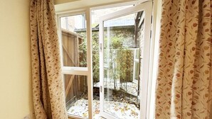 A room with a sliding glass door leading to a garden with plants and a small pond. - Charming Notting Hill Mews House (London)