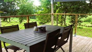 Eine Holzdachterrasse mit Tisch und Stühlen, einem überdachten Bereich und Blick auf eine grüne Landschaft.