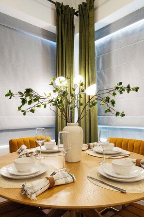 Enjoy meals in this stylish dining area with a round table, white tableware, and a vase with greenery.