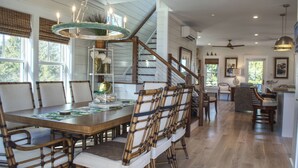 Un comedor amplio con una gran mesa de madera y sillas, una escalera con barandillas de madera y un ventilador de techo.