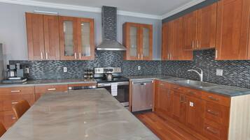 Una cocina moderna con armarios de madera, una isla grande, electrodomésticos de acero inoxidable y un revestimiento de pared de azulejos negros.