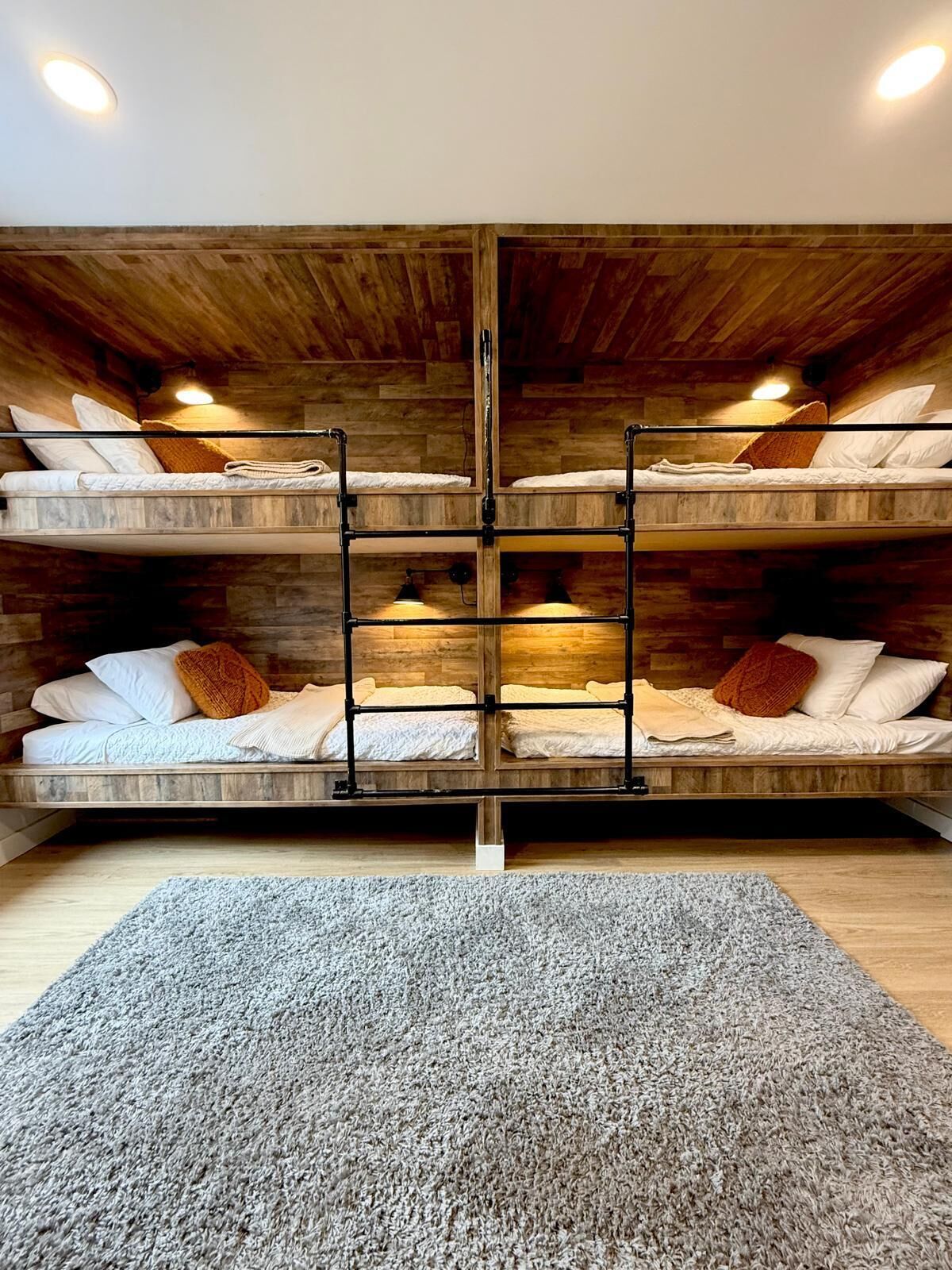 A loft-style bedroom with a wooden ceiling and exposed beams, featuring two bunk beds with white bedding and orange throw pillows.