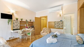 A hotel room with a bed, a desk, a chair, a TV, and a shower area. - Sonia Sweet Love With Shared Pool (Gardone Riviera)