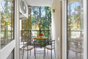 A balcony with a table and chairs, a fan, and a view of trees and buildings. - Sonia Sweet Love With Shared Pool (Gardone Riviera)
