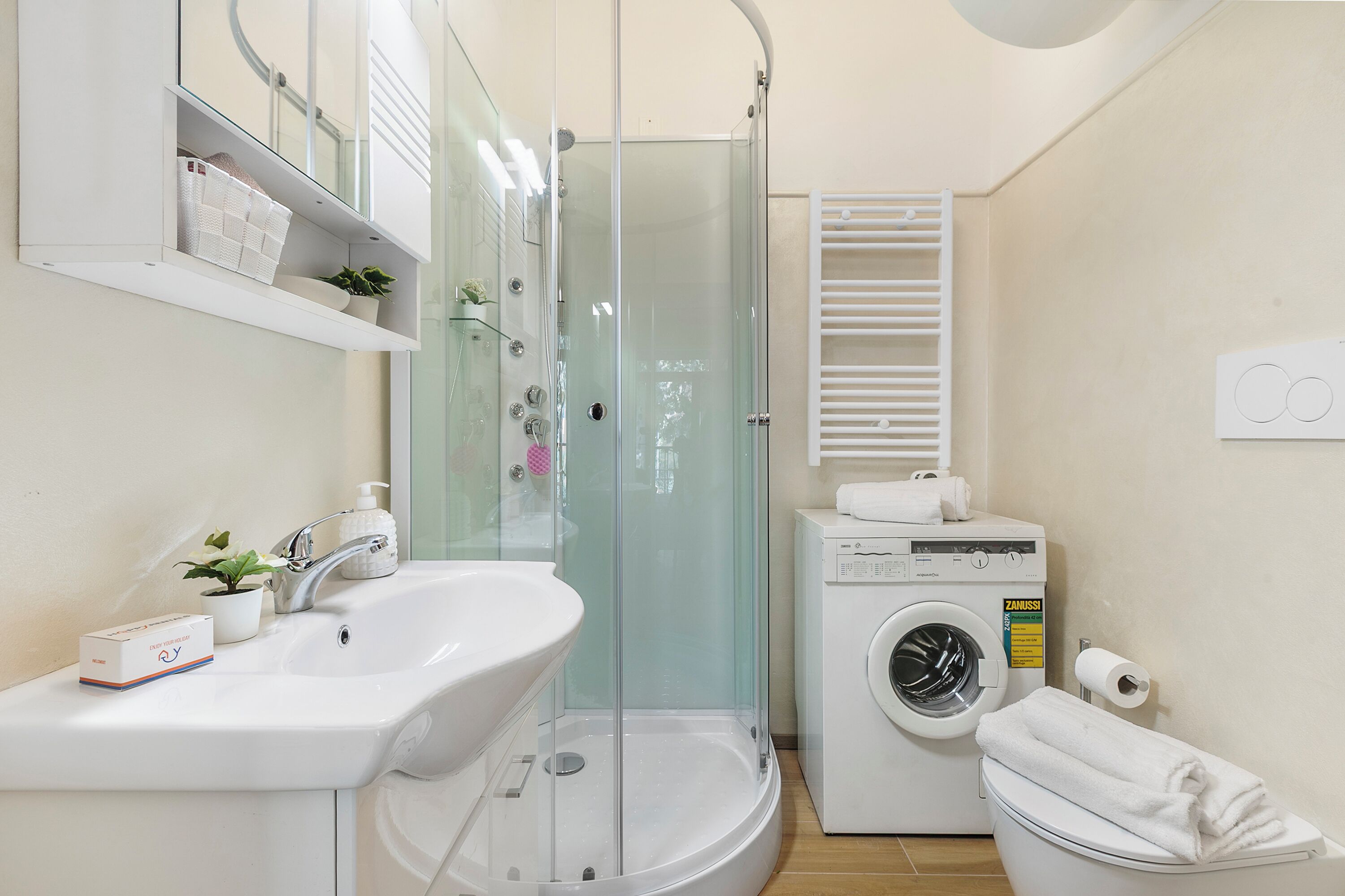 Un bagno moderno con doccia vetro, lavandino, lavatrice e WC.