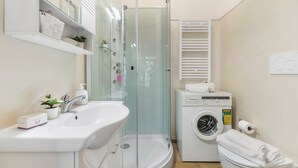 A modern bathroom with a glass-enclosed shower, a sink, a washing machine, and a toilet. - Sonia Sweet Love With Shared Pool (Gardone Riviera)