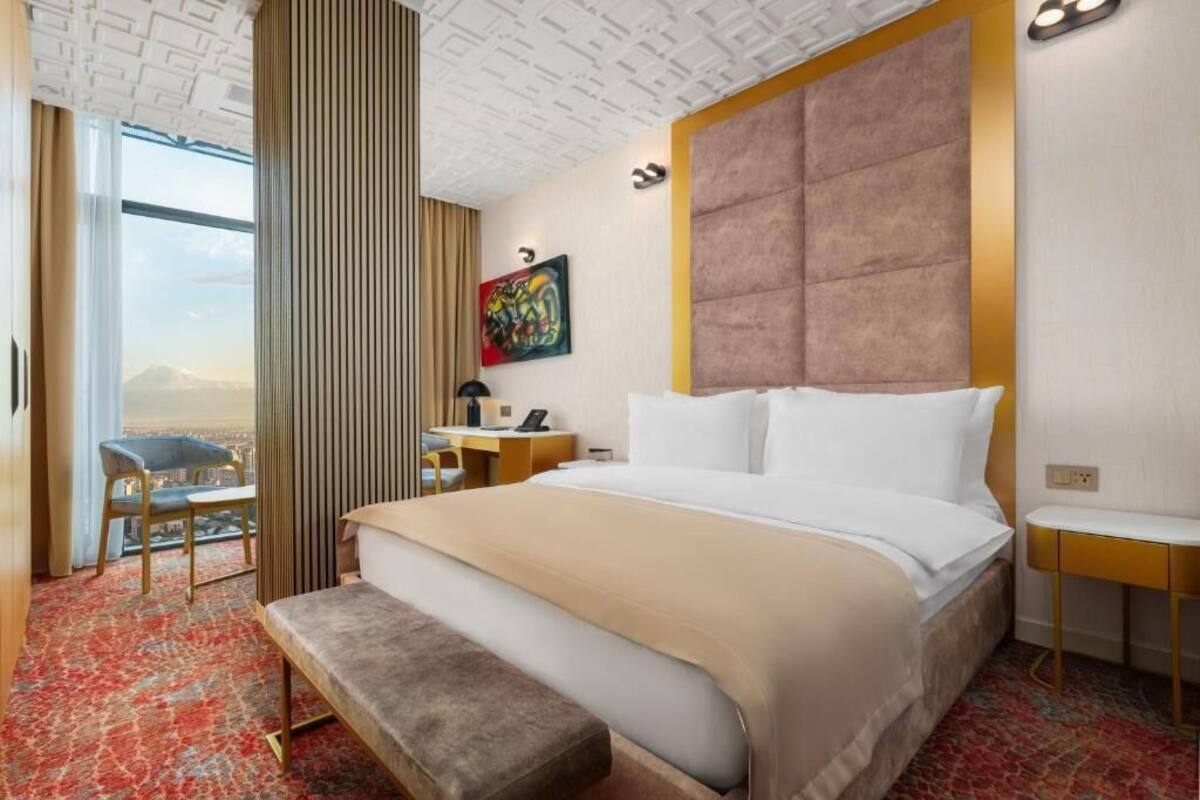 A hotel room with a large bed, a desk, a chair, and a view of the city.