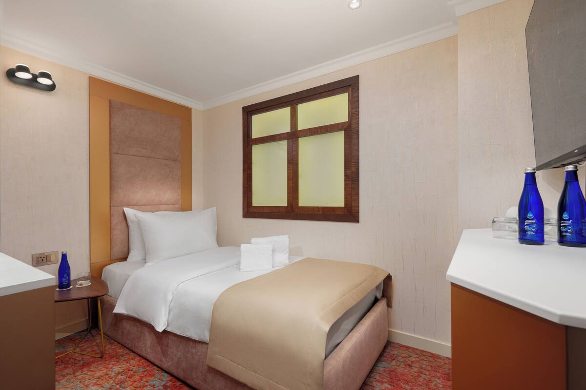 A hotel room with a bed, bedside table, and a window with blinds.
