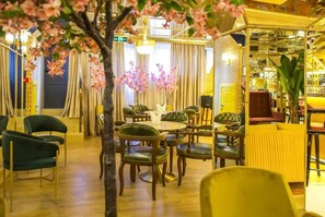 A restaurant with round tables and chairs, a tree with pink flowers, and a yellow wall.
