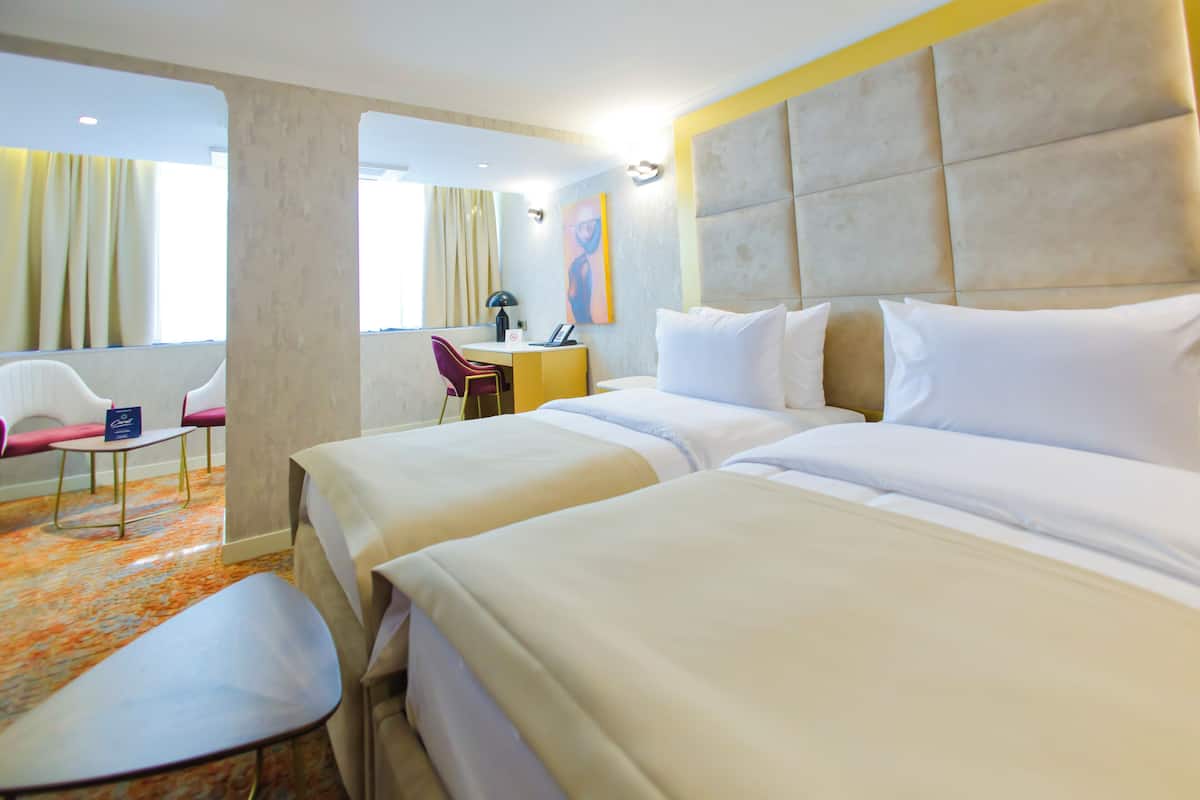A hotel room with two beds, a desk, a chair, and a large window.