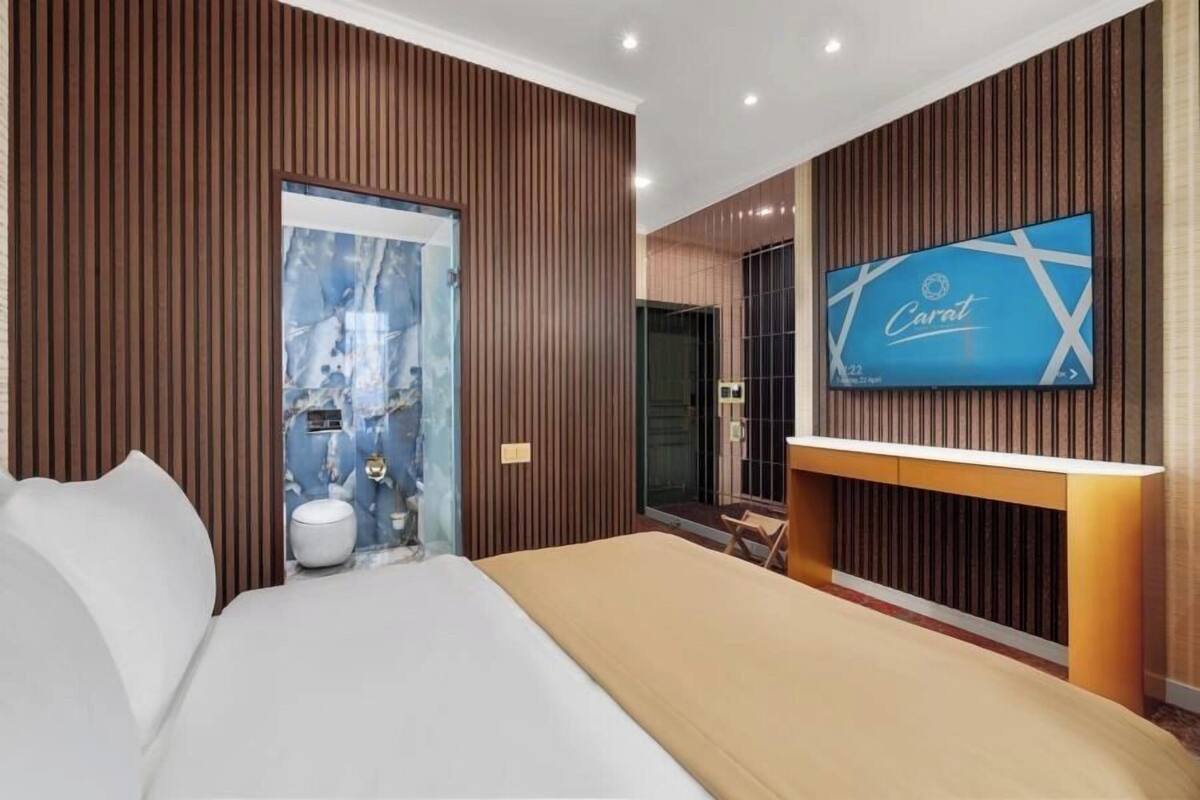 A modern hotel room with a large bed, a television mounted on the wall, and a wooden panel design.