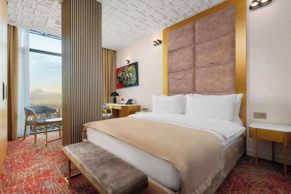 A hotel room with a large bed, a desk, a chair, and a view of the city.