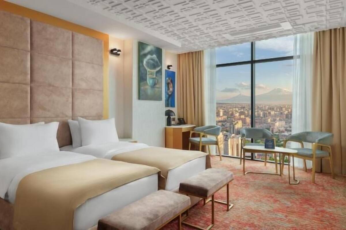 A hotel room with a large bed, a desk, a chair, and a view of a cityscape.