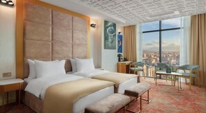 A hotel room with a large bed, a desk, a chair, and a view of a cityscape.