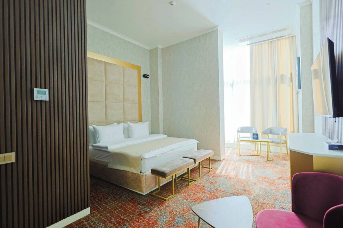 A hotel room with a bed, a bench, a desk, a chair, and a television.