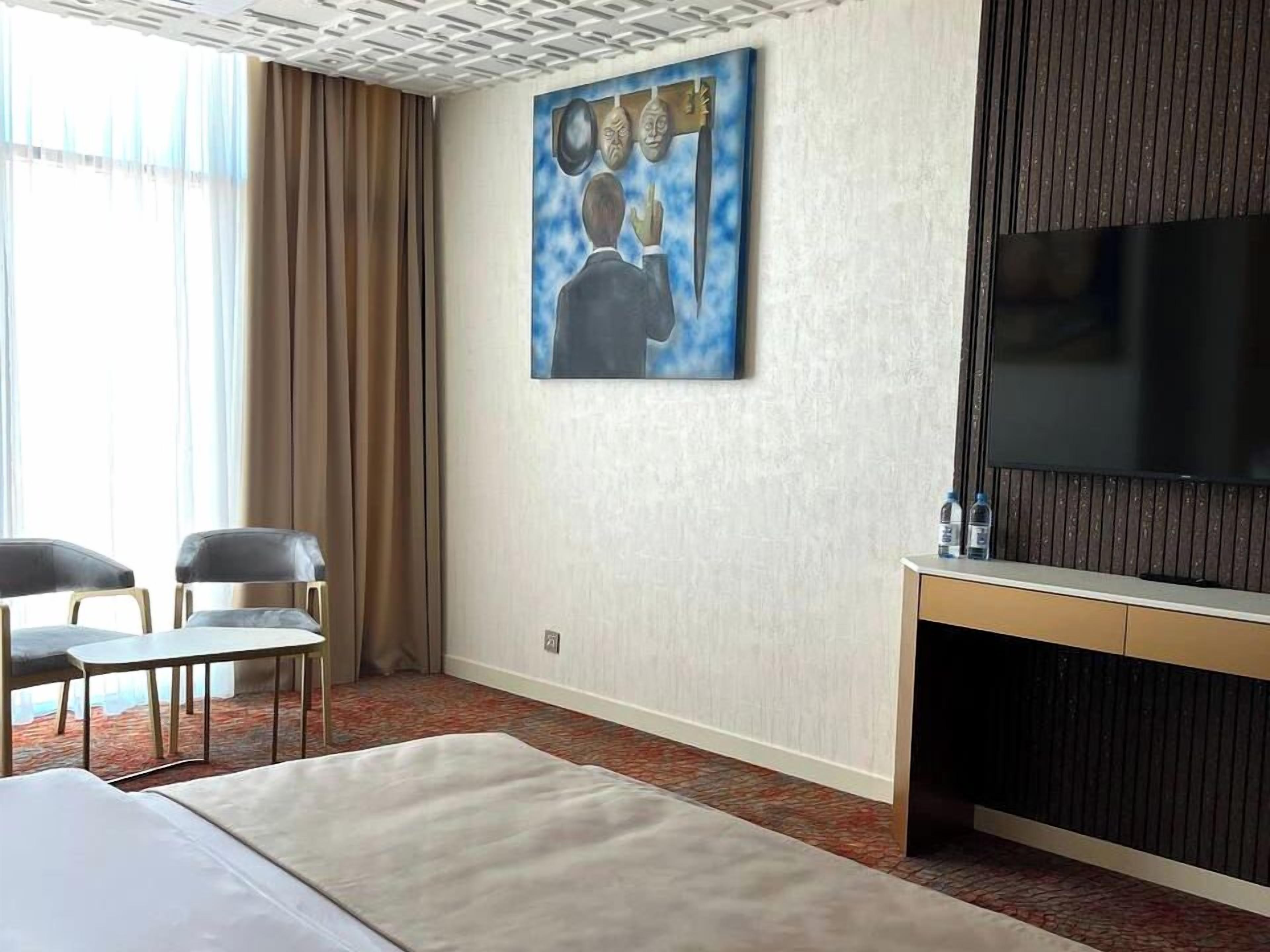 Et hotelværelse med seng, fjernsyn, et billede på væggen og et vindue med gardiner.