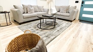 A living room with a grey sofa, a coffee table, a floor lamp, and a large window with blinds. - The Haven Hideaway in Atlanta (Atlanta)