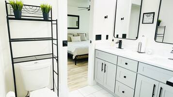 A modern bathroom with a toilet, sink, and mirror. There is a black metal shelf with plants and a black rug on the floor.