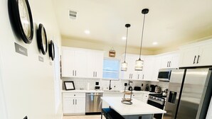 A modern kitchen with white cabinets, a stainless steel refrigerator, and a central island with bar stools. - The Haven Hideaway in Atlanta (Atlanta)