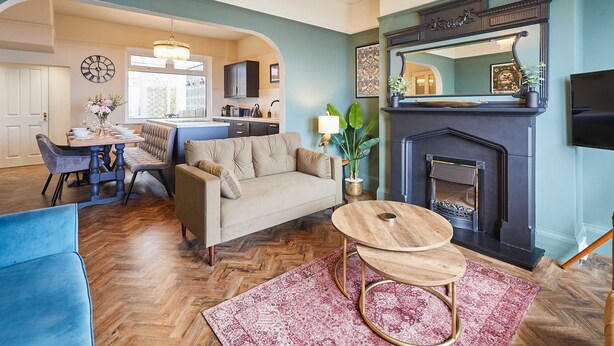 A living room with a sofa, coffee table, and fireplace. There is a dining area with a table and chairs. The room has wooden flooring and a large mirror above the fireplace. - Host Stay Twelve On The Terrace (Newbiggin-by-the-Sea)