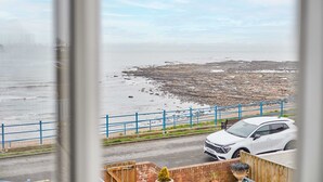 A coastal view with a white SUV parked near a blue railing, overlooking rocky terrain and the sea. - Host Stay Twelve On The Terrace (Newbiggin-by-the-Sea)