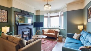 A living room with a fireplace, two sofas, a television, and a chandelier. - Host Stay Twelve On The Terrace (Newbiggin-by-the-Sea)