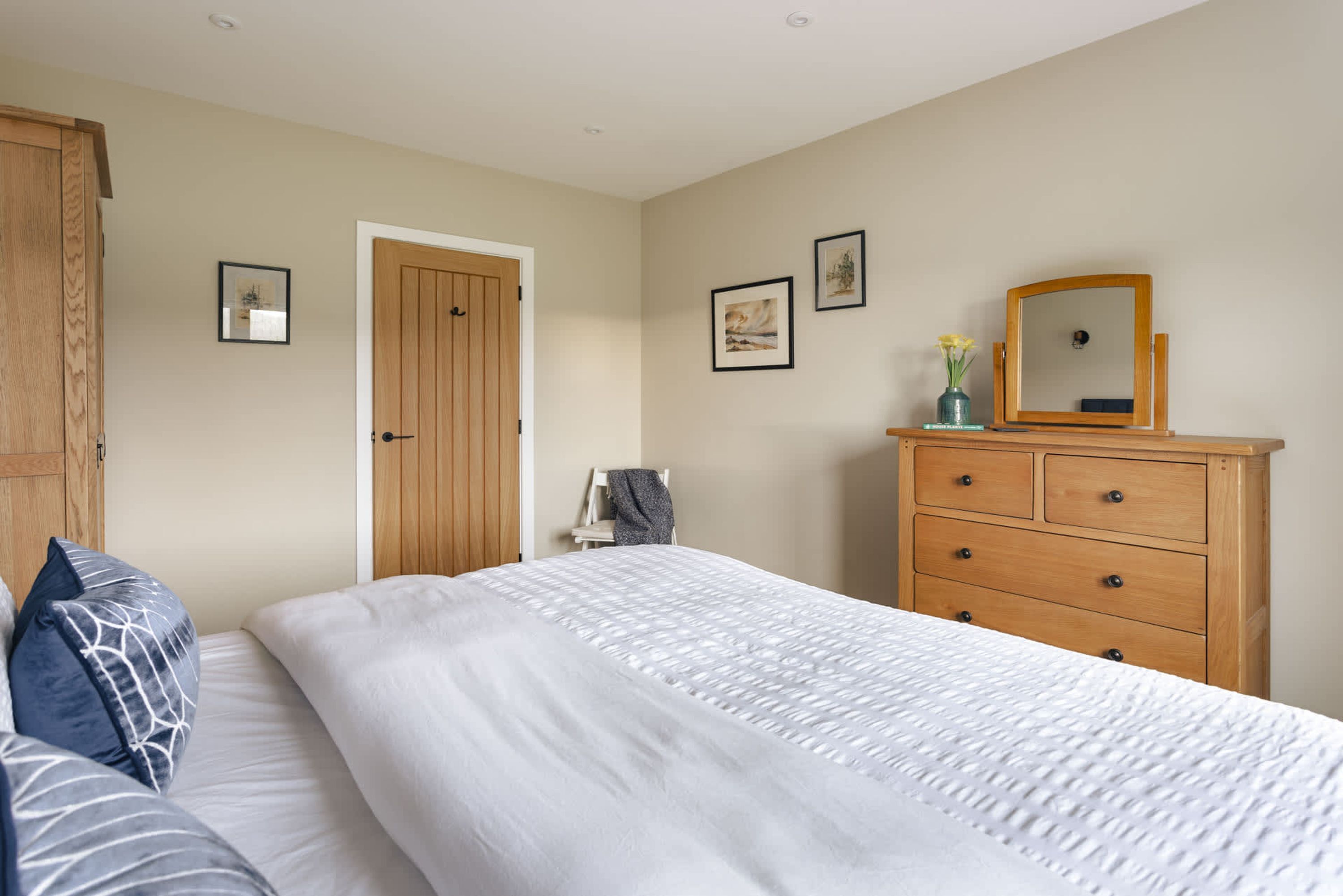 Een slaapkamer met een bed, een houten dressoir en ingekaderde foto’s aan de muur.
