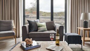 A modern living room with a grey sofa, a coffee table with a book and a wine glass, and a view of a stone landscape through large windows. - Lily Bank in Staveley (Kendal)