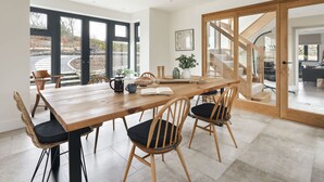 A modern dining area with a wooden table and chairs, a large window with a view of the outdoors, and a staircase leading to another level. - Lily Bank in Staveley (Kendal)
