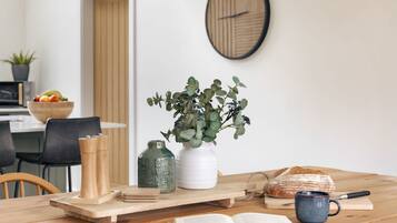 Una mesa de madera con un libro, una taza, un pan y un florero con plantas verdes.