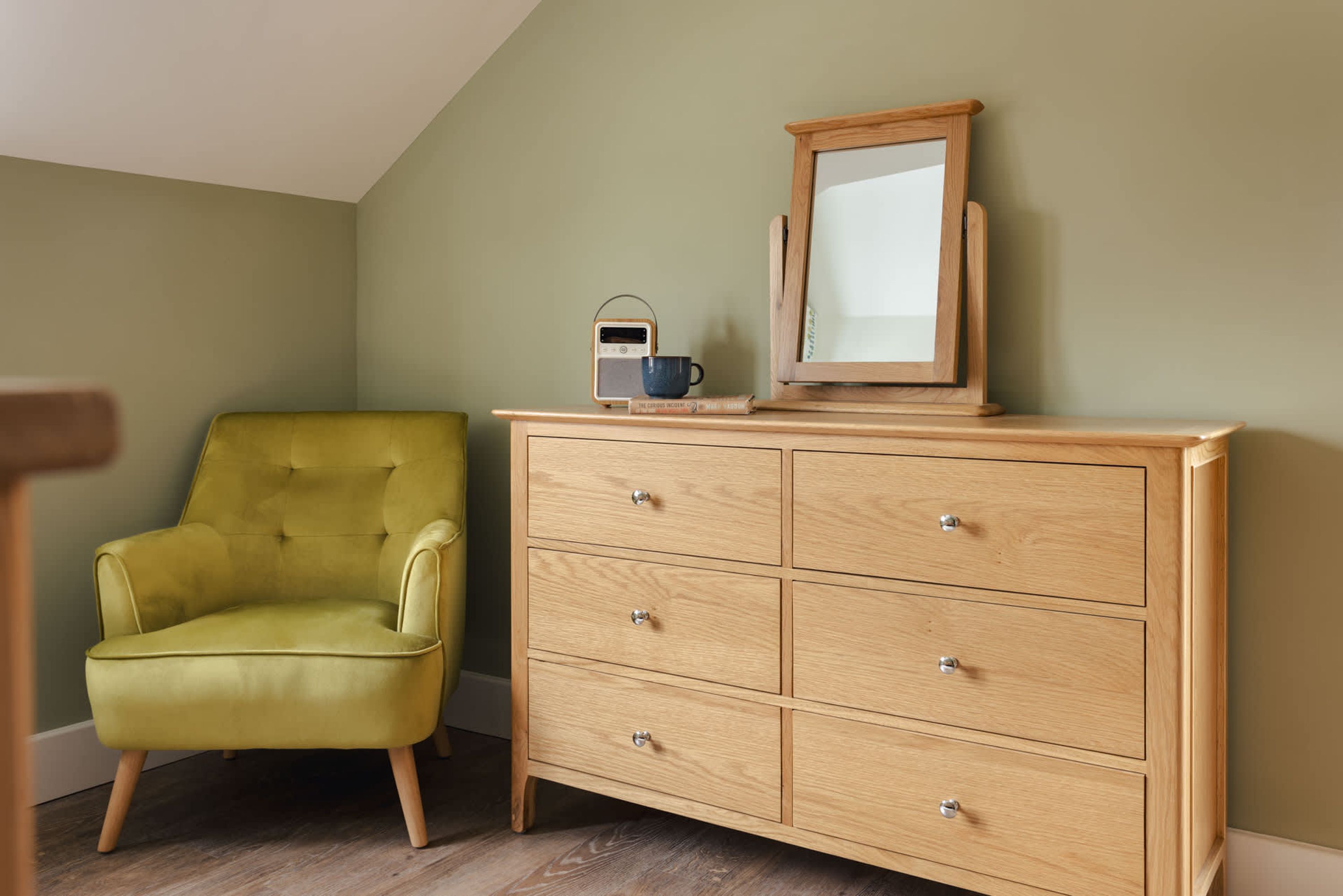 Une pièce avec une commode en bois, un fauteuil vert et une radio posée sur la commode.