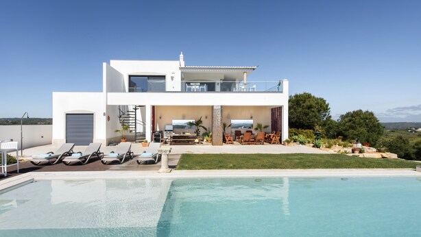 Una casa moderna de dos pisos con piscina, mobiliario exterior y vistas al paisaje.