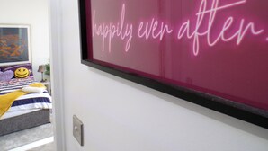 A bedroom with a bed, a framed neon sign on the wall, and a window. - Apartmentsleeps4-west Kensington-petsok-parking (London)