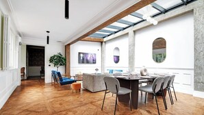 A spacious dining area with a wooden herringbone floor, a round table set for six, and a large window with a view of greenery. - A PERFECT BLEND OF CLASSIC ELEGANCE & MODERN COMFORT NEXT TO LUXEMBOURG GARDEN (Paris)